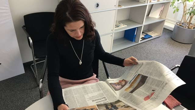 Eine Frau in schwarzem Oberteil sitzt an einem Tisch und blickt in eine Ausgabe des Tages-Anzeigers. Eine Frau in schwarzem Oberteil sitzt an einem Tisch und blickt in eine Ausgabe des Tages-Anzeigers.