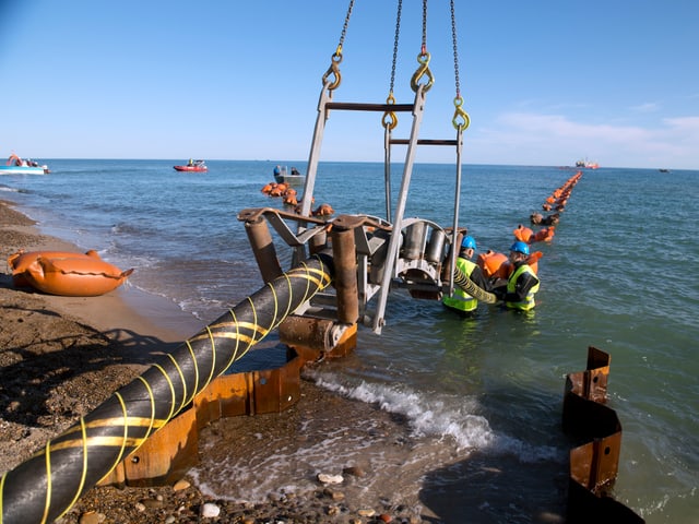 Ein paar Arbeiter verlegen ein dickes Stromkabel ins Wasser. Ein paar Arbeiter verlegen ein dickes Stromkabel ins Wasser.