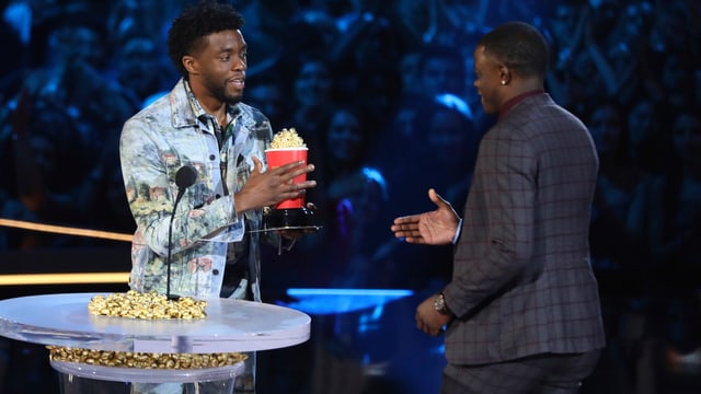 Zwei Männer, die sich einen Pocpcornbecher mti goldenem Popcorn überreichen. Zwei Männer, die sich einen Pocpcornbecher mti goldenem Popcorn überreichen.