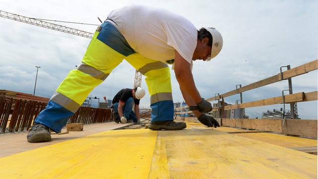 Bauarbeiter auf einer gelben Holzplatte. Er bückt sich. Bauarbeiter auf einer gelben Holzplatte. Er bückt sich.
