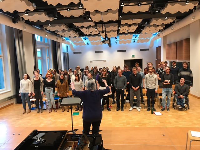 Etwa 50 Chormitglieder singen zusammen. Vorne eine Dirigentin. Etwa 50 Chormitglieder singen zusammen. Vorne eine Dirigentin.
