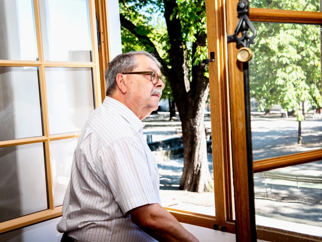 Ein älterer Herr mit Brille und Schnauz schaut aus dem geöffneten Fenster. Ein älterer Herr mit Brille und Schnauz schaut aus dem geöffneten Fenster.