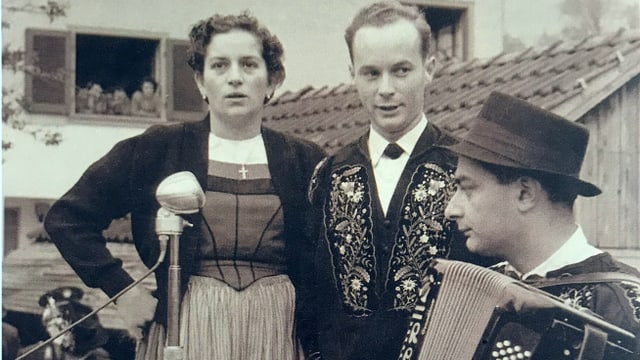 Schwarz-Weiss-Fotografie von einem singenden Paar, das von einem Akkordeonisten begleitet wird. Schwarz-Weiss-Fotografie von einem singenden Paar, das von einem Akkordeonisten begleitet wird.