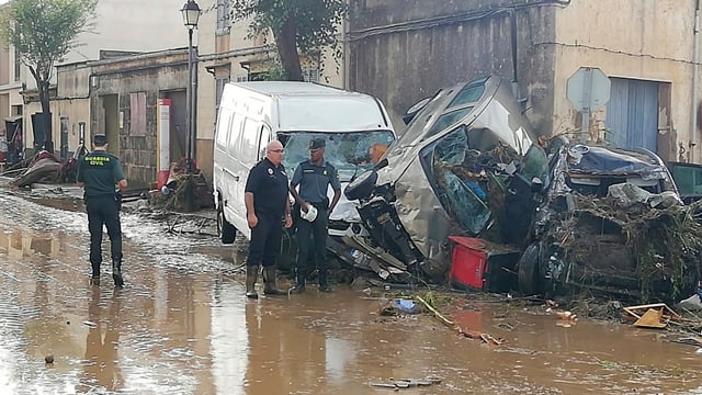 Polizisten schauen sich auf einer überfluteten Strasse kaputte Autos an. Polizisten schauen sich auf einer überfluteten Strasse kaputte Autos an.