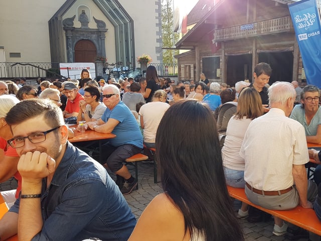 Voll besetzte Festbänke vor einem Chalet.