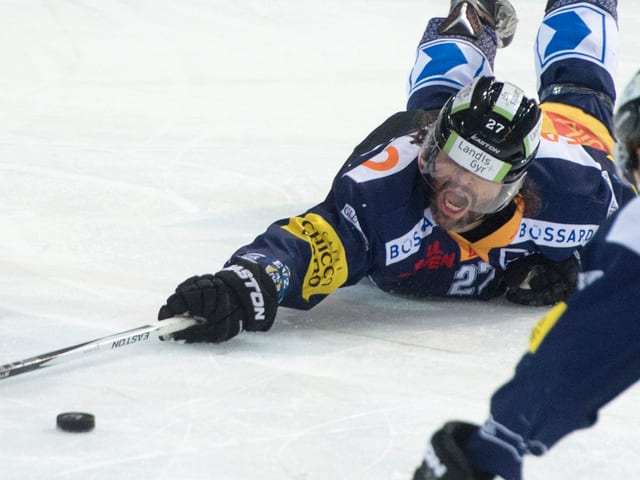 Zugs Josh Holden liegt bäuchlings auf dem Eis und streckt sich mit letztem Einsatz nach der Scheibe.