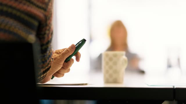 Gespräch an einem Tisch, im Vordergrund Mann mit Stift in der Hand Gespräch an einem Tisch, im Vordergrund Mann mit Stift in der Hand