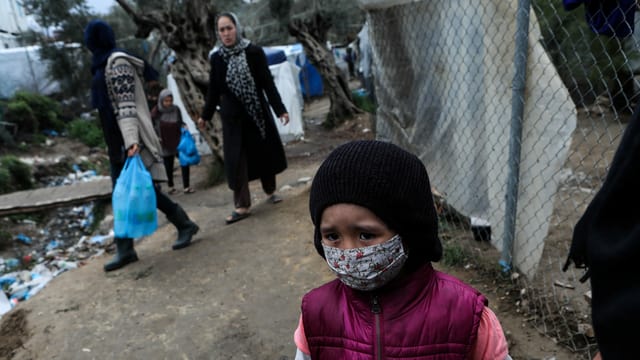 Menschen in Moria, im Vordergrund ein Kind mit Gesichtsmaske. Menschen in Moria, im Vordergrund ein Kind mit Gesichtsmaske.