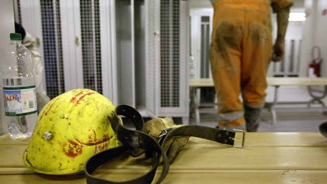Umkleidekabine auf Baustelle: Mineralwasserflasche, gelber Helm und ein Ledergürtel auf einer Bank. Umkleidekabine auf Baustelle: Mineralwasserflasche, gelber Helm und ein Ledergürtel auf einer Bank.