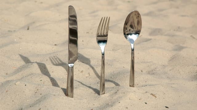Messer, Gabel und Löffel stecken in Sand. Messer, Gabel und Löffel stecken in Sand.