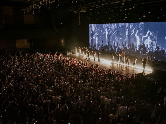 Konzerthalle, Publikum im Vordergrund, hinten die Bühne mit Band und LED-Screen Konzerthalle, Publikum im Vordergrund, hinten die Bühne mit Band und LED-Screen