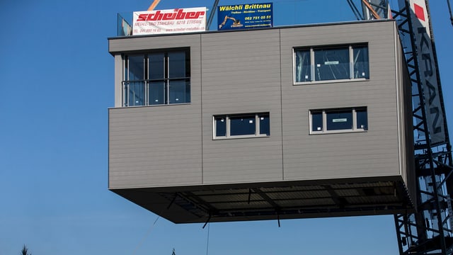 Das Haus wird vom Kran angehoben und schwebt zu seinem endgültigen Standort auf dem Silo. Das Haus wird vom Kran angehoben und schwebt zu seinem endgültigen Standort auf dem Silo.