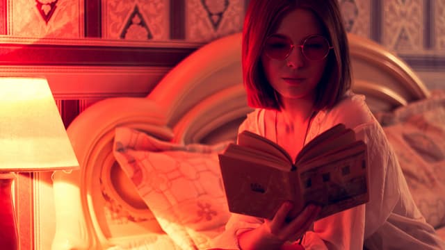 eine junge Frau mit Brille liest im Bett ein Buch