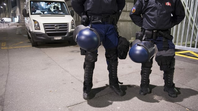 Zwei Polizisten stehen in Schutzmontur vor einem Polizeiauto. Zwei Polizisten stehen in Schutzmontur vor einem Polizeiauto.