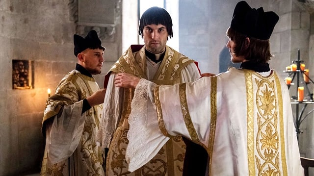 Zwingli im Priestergewand. Zwei Kollegen helfen ihm, die Stola zu richten. Zwingli im Priestergewand. Zwei Kollegen helfen ihm, die Stola zu richten.