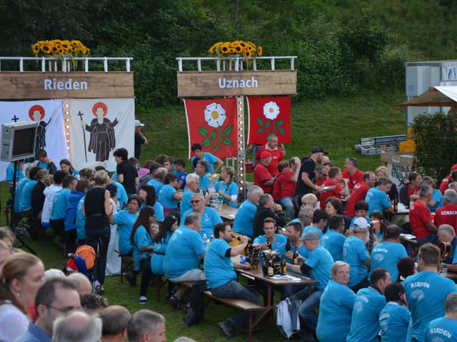 Festbänke mit rot und blau gekleideten Menschen.