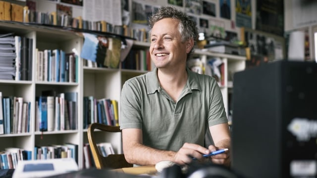 Ein Mann sitzt an seinem Pult in seinem Büro. Hinter ihm viele Bücher, CDs und Fotos. Ein Mann sitzt an seinem Pult in seinem Büro. Hinter ihm viele Bücher, CDs und Fotos.