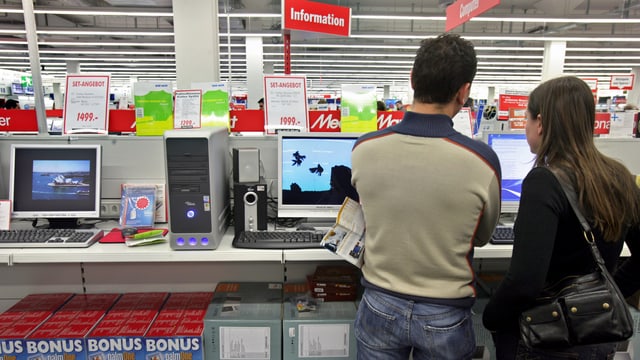 Kunden stehen in einem Medienmarkt vor dem Regal mit Computern Kunden stehen in einem Medienmarkt vor dem Regal mit Computern
