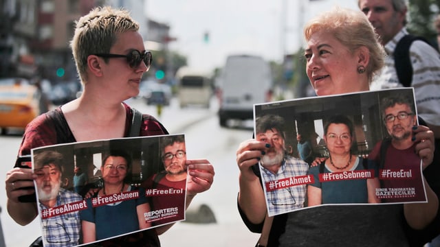 Zwei Demonstrantinnen halten Plakate hoch, darauf die drei verhafteten Journalisten. Zwei Demonstrantinnen halten Plakate hoch, darauf die drei verhafteten Journalisten.