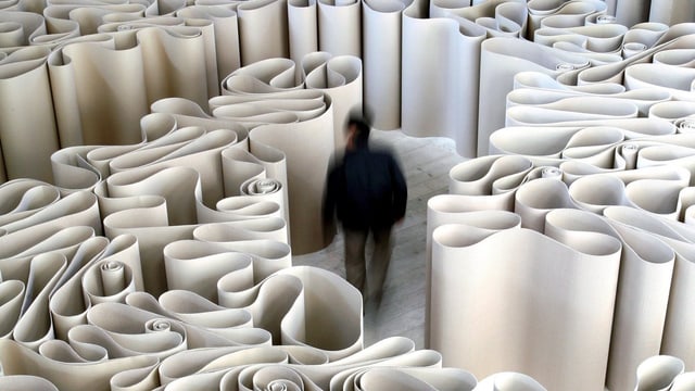 Mann geht durch ein Labyrinth aus hochkant aufgestellten Papierbögen. Mann geht durch ein Labyrinth aus hochkant aufgestellten Papierbögen.