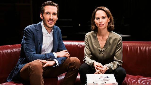 Ein Mann und eine Frau sitzen auf einem Sofa und blicken in die Kamera Ein Mann und eine Frau sitzen auf einem Sofa und blicken in die Kamera