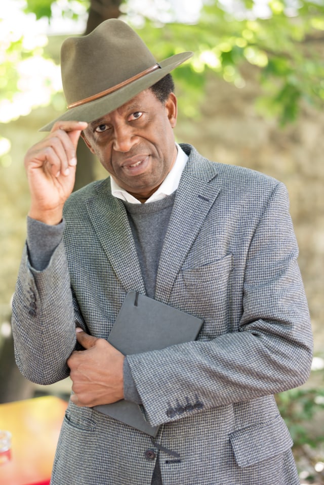 Dany Laferrière im Anzug, mit einem Buch im Arm, guckt in die Kamera. Dany Laferrière im Anzug, mit einem Buch im Arm, guckt in die Kamera.