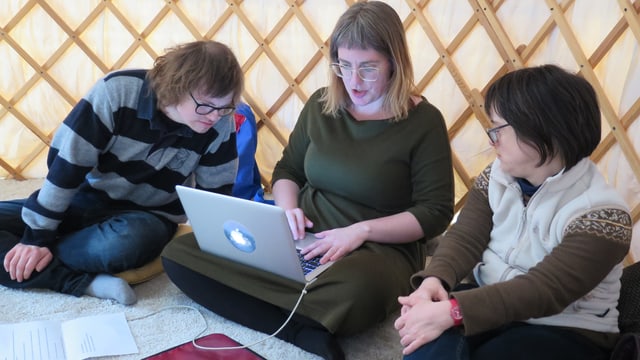 Ein Mann und eine Frau blicken einer Frau in ihrer Mitte über die Schulter, die etwas auf einem Computer schreibt Ein Mann und eine Frau blicken einer Frau in ihrer Mitte über die Schulter, die etwas auf einem Computer schreibt