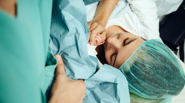 Eine Frau im Gebärsaal hält das Händchen ihres Neugeborenen.