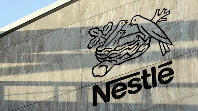 Das Firmenlogo von Nestlé an einer grauen Hausmauer. Das Firmenlogo von Nestlé an einer grauen Hausmauer.