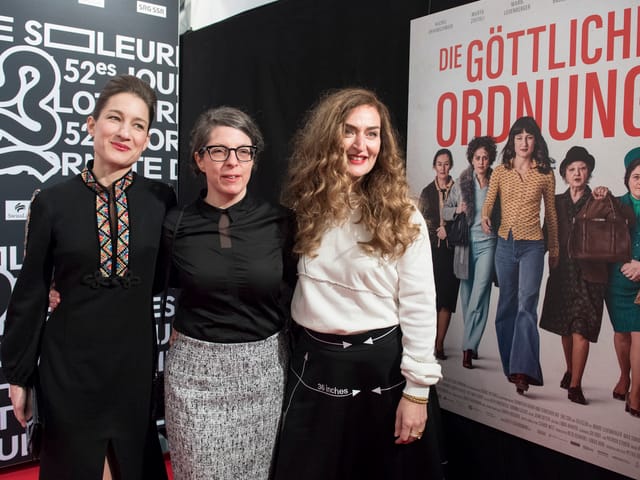 Drei Frauen stehen vor einem Werbeplakat. Drei Frauen stehen vor einem Werbeplakat.