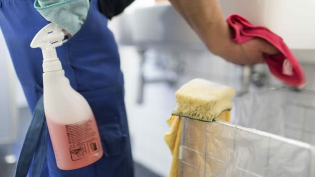 Ein Angestellter einer Reinigungsfirma putzt ein Wachbecken Ein Angestellter einer Reinigungsfirma putzt ein Wachbecken