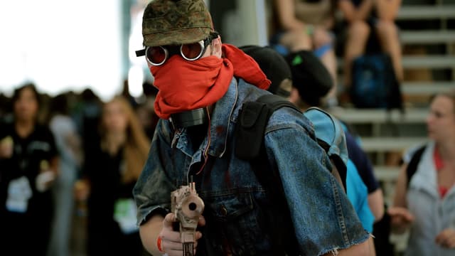 Ein vermummter Mann mit Staub-Brille zielt mit seiner Plastikpistole auf uns.