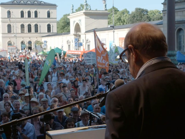 Jean Ziegler von hinten bei einem Auftritt vor einer grossen Menschenmenge. Jean Ziegler von hinten bei einem Auftritt vor einer grossen Menschenmenge.