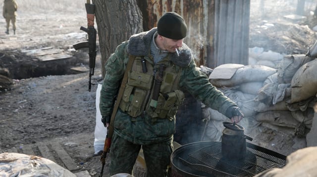 Ein Mann in Militärkleidunhg kontrolliert einen Wasserkessel auf einer Feuerstelle