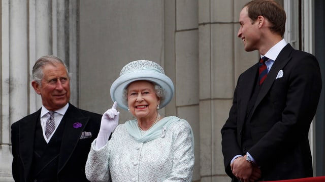 Queen auf einem Balkon, sie winkt. Daneben Charles und William. Queen auf einem Balkon, sie winkt. Daneben Charles und William.