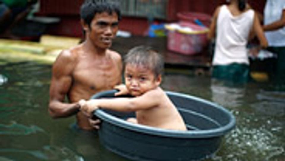 Ein Mann transportiert sein Kind durch die Fluten südlich von Manila (Philippinen).