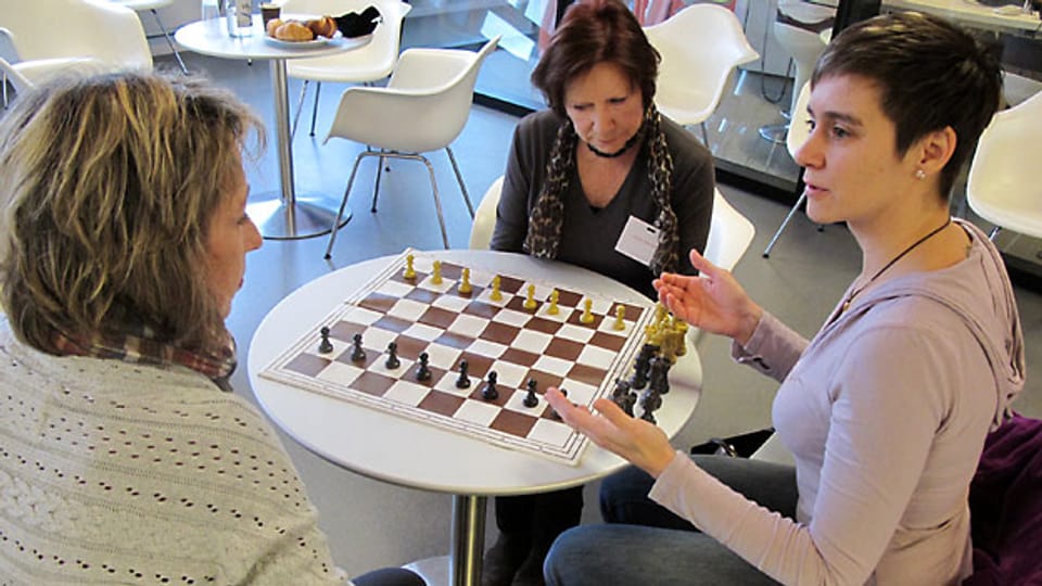 Die beiden Hörerinnen Anita Gaggioli (links) und Margrit Freiermuth (mitte) lernen Schach spielen. Rahel Umbach erklärt die Spielregeln.