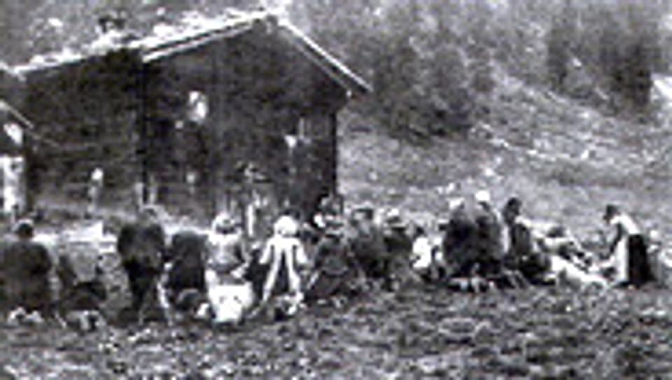 Walliser Bettler finden sich auf einer Alp im Turtmanntal ein. Sie warten auf den Knien. Bevor sie ihr Käsestück bekommen haben sie mit dem Alpvogt zu beten. Ein Bild aus der 30er-Jahren.