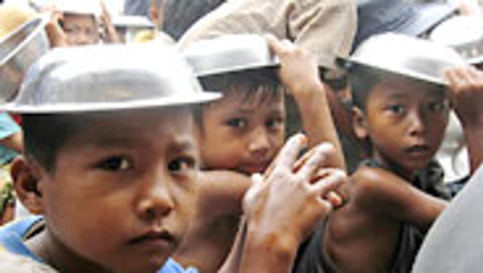 Kinder in Burma warten im Regen auf einen Teller Reis.