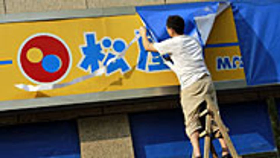 Ein Arbeiter in Shanghai verdeckt die japanische Beschriftung eines Restaurants