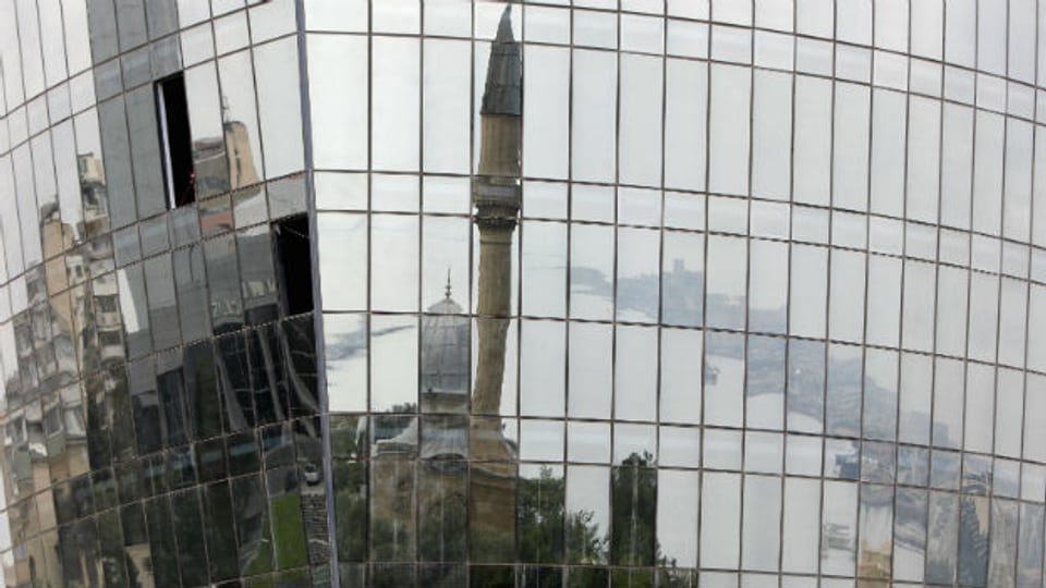 Moschee und Häuserfronten widerspiegeln sich in der Fassade eines Hochhauses in Baku.