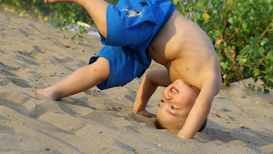 Arme am Boden, Hinterteil in der Höhe: Ein Kind schlägt im Sand einen Purzelbaum.