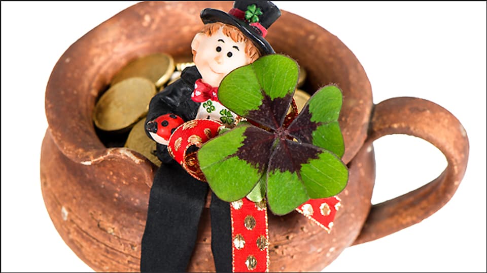 Versprechen jede Menge Glück: Ein Kaminfeger mit einem vierblättrigen Kleeblatt auf einem Topf voller Münzen.