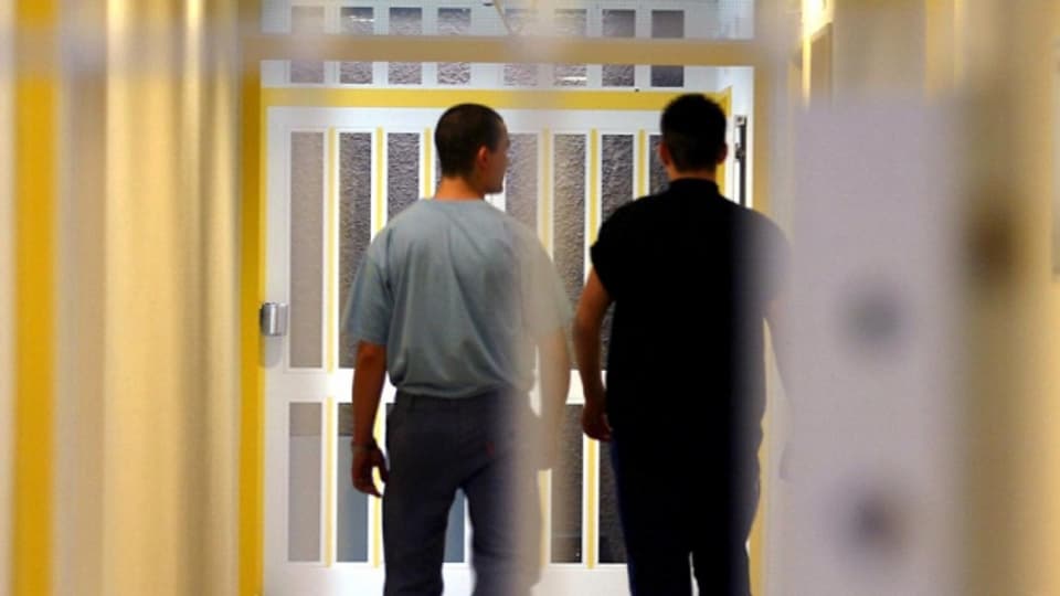 Zwei Männer in einem Gang. Im Vordergrund Gitter