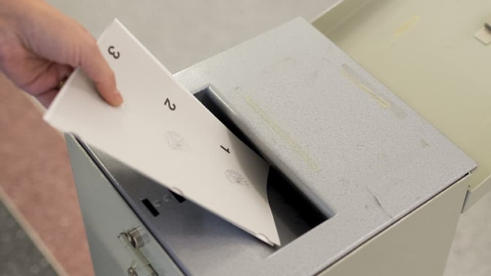Eine Person wirft einen Zettel in eine Wahlurne