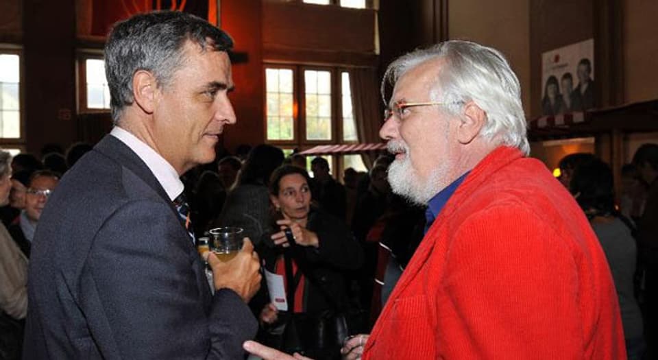 Sein roter Kittel ist sein Markenzeichen: Urs Müller im Gespräch mit Regierungspräsident Guy Morin.