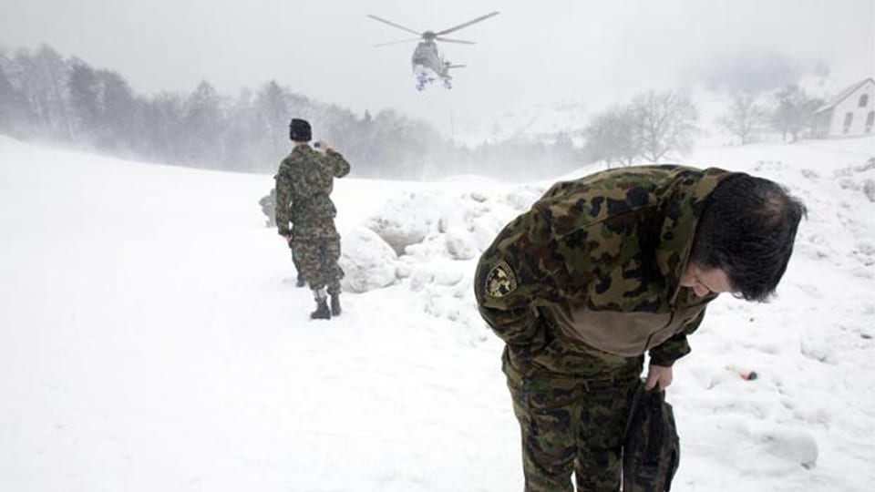 Zwei Soldaten ducken sich, weil ein Helikopter im Schnee landet und Schnee aufwirbelt.