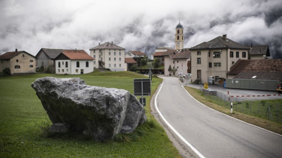 Ein grosser Stein liegt vor dem Dorf, der Tag nebelverhangen.