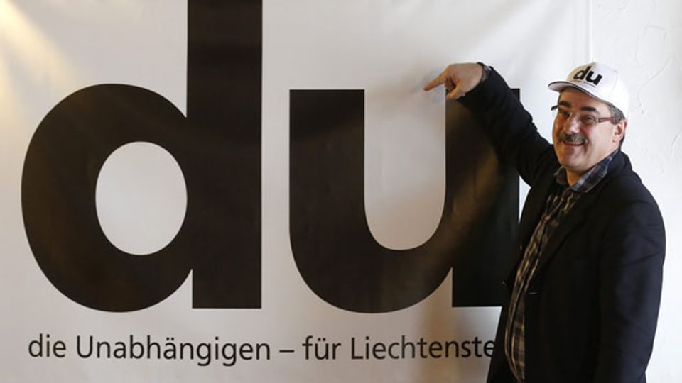 Ein Politiker posiert vor einem DU-Plakat.
