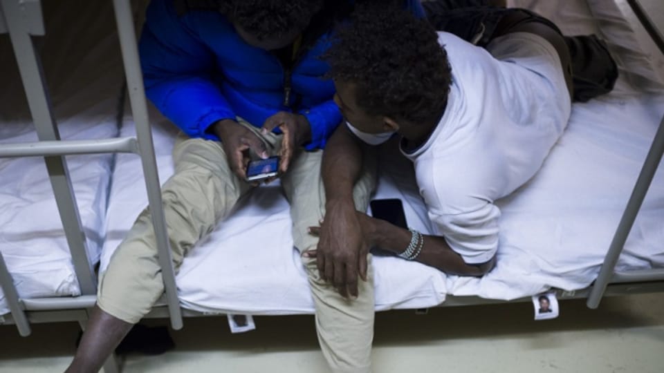 Zwei Asylbewerber in einer Unterkunft schauen auf ein Smartphone